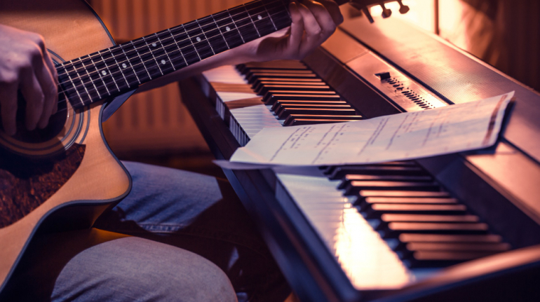 man-playing-acoustic-guitar-and-piano-close-up-recording-notes-beautiful-color-background-music-activity-concept